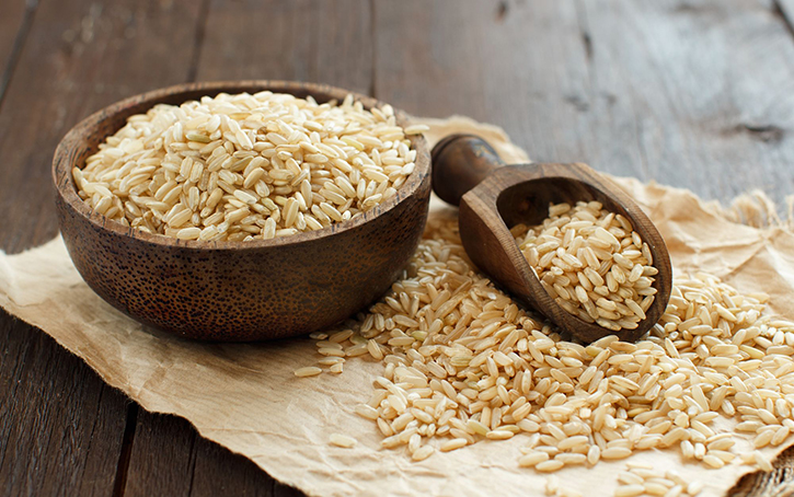 Pile of Brown rice in a bowl with a wooden spoon close up